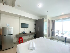A hotel room with a bed, a TV mounted on the wall, a minibar, a red stool, and a balcony with a view.