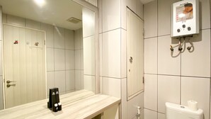 A bathroom with a mirror, a toilet, and a wall-mounted heater. - Enjoy Living Studio Room At High Floor Grand Kamala Lagoon Apartment (Bekasi)