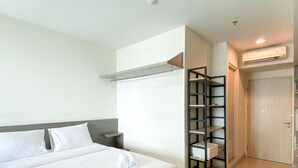 A hotel room with a bed, a nightstand, a built-in shelf, and a wardrobe. - Enjoy Living Studio Room At High Floor Grand Kamala Lagoon Apartment (Bekasi)