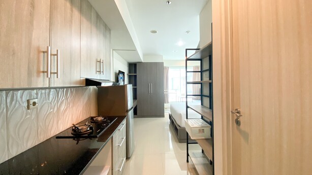 A modern kitchen with wooden cabinets, a black countertop, and a built-in oven. - Enjoy Living Studio Room At High Floor Grand Kamala Lagoon Apartment (Bekasi)