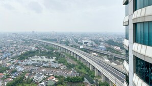 A high-rise building with a view of a cityscape, including a bridge and a river. - Enjoy Living Studio Room At High Floor Grand Kamala Lagoon Apartment (Bekasi)