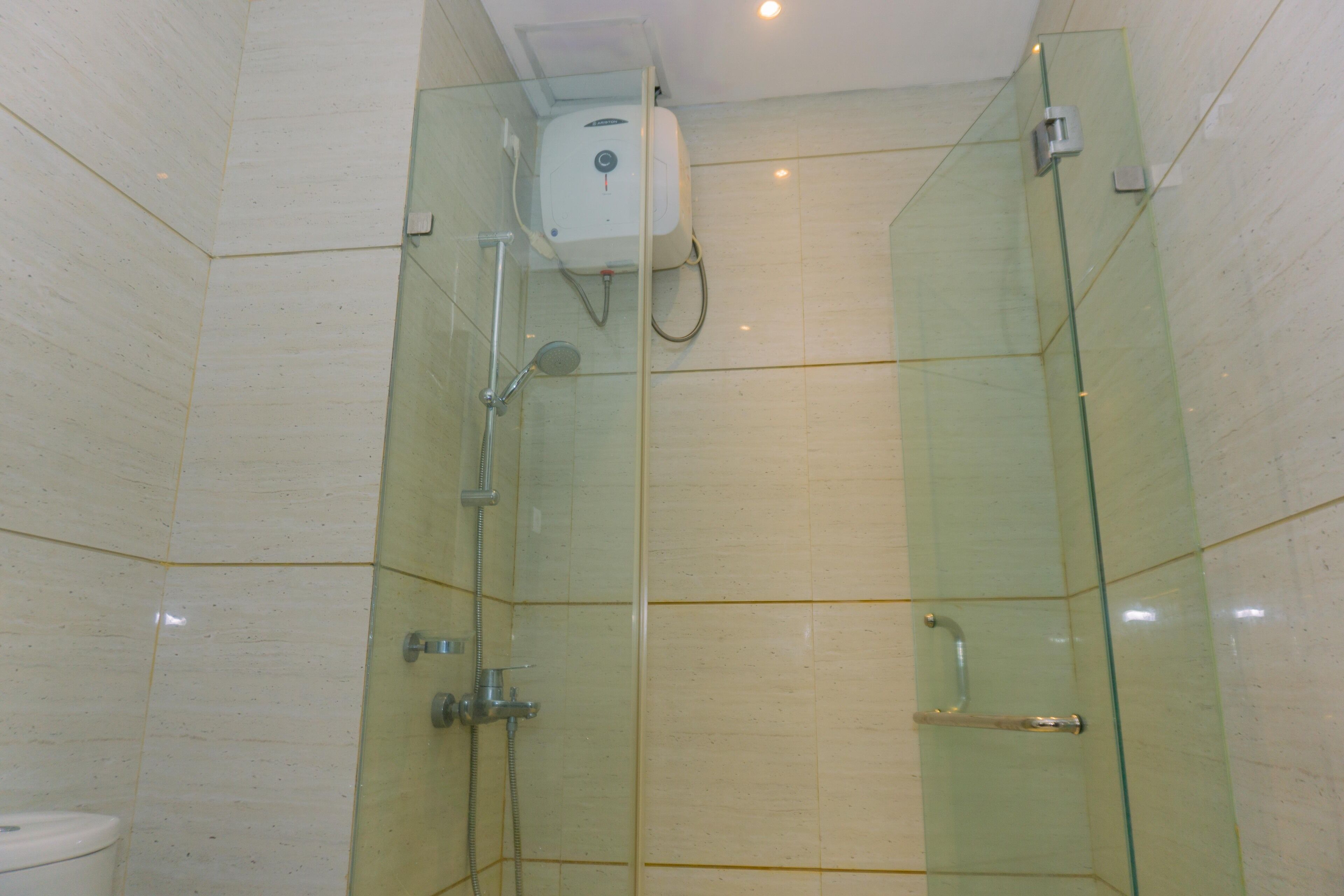 Cabina de ducha con paredes de vidrio, cabezal de ducha de mano, llave de pared y puerta de cristal.