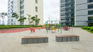 A playground with various play equipment, surrounded by a paved area with benches and greenery.