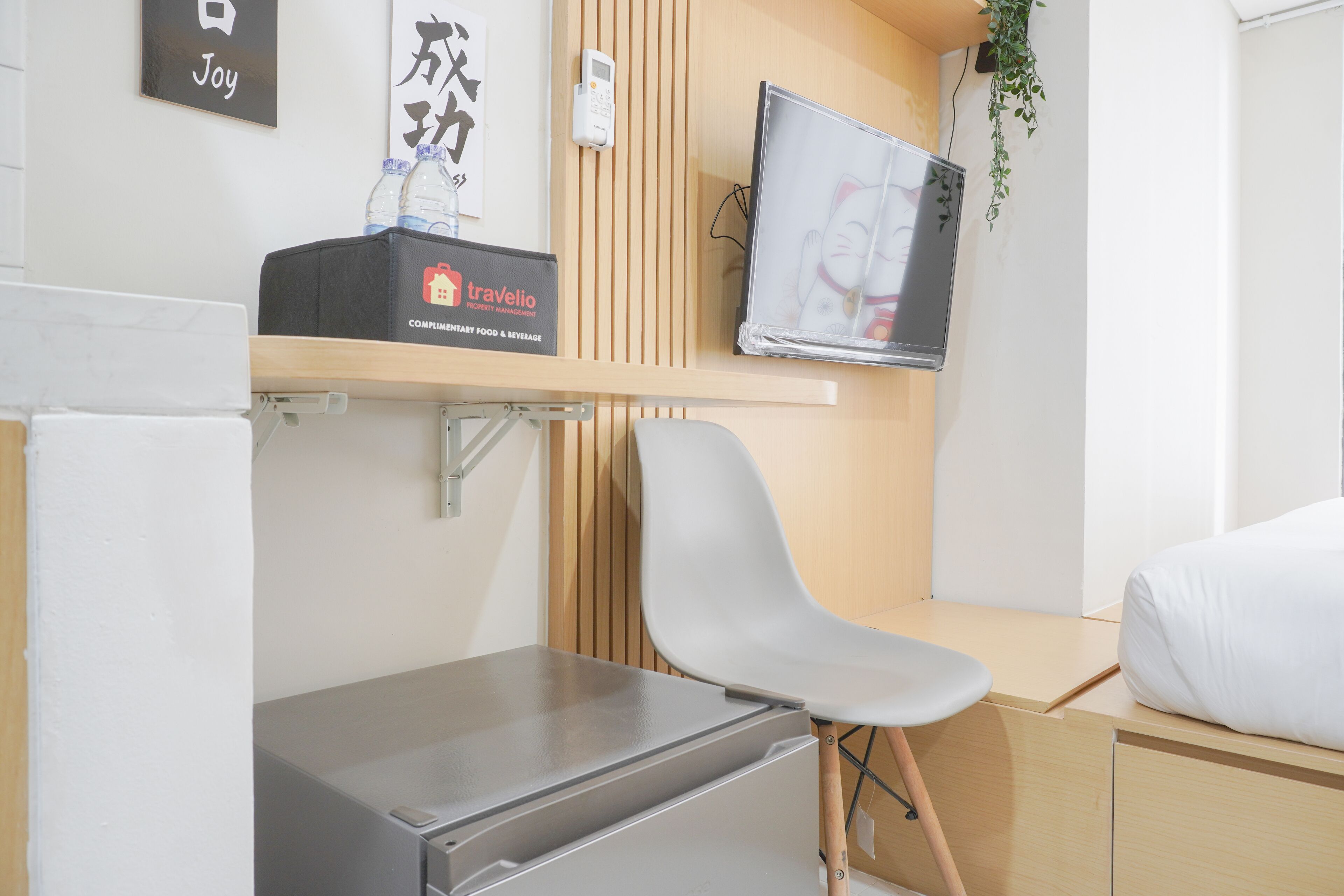 A modern hotel room with a bed, a desk, a chair, a TV, and a minibar.