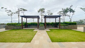 A covered outdoor area with two wooden pergolas, surrounded by well-maintained grass and low hedges.