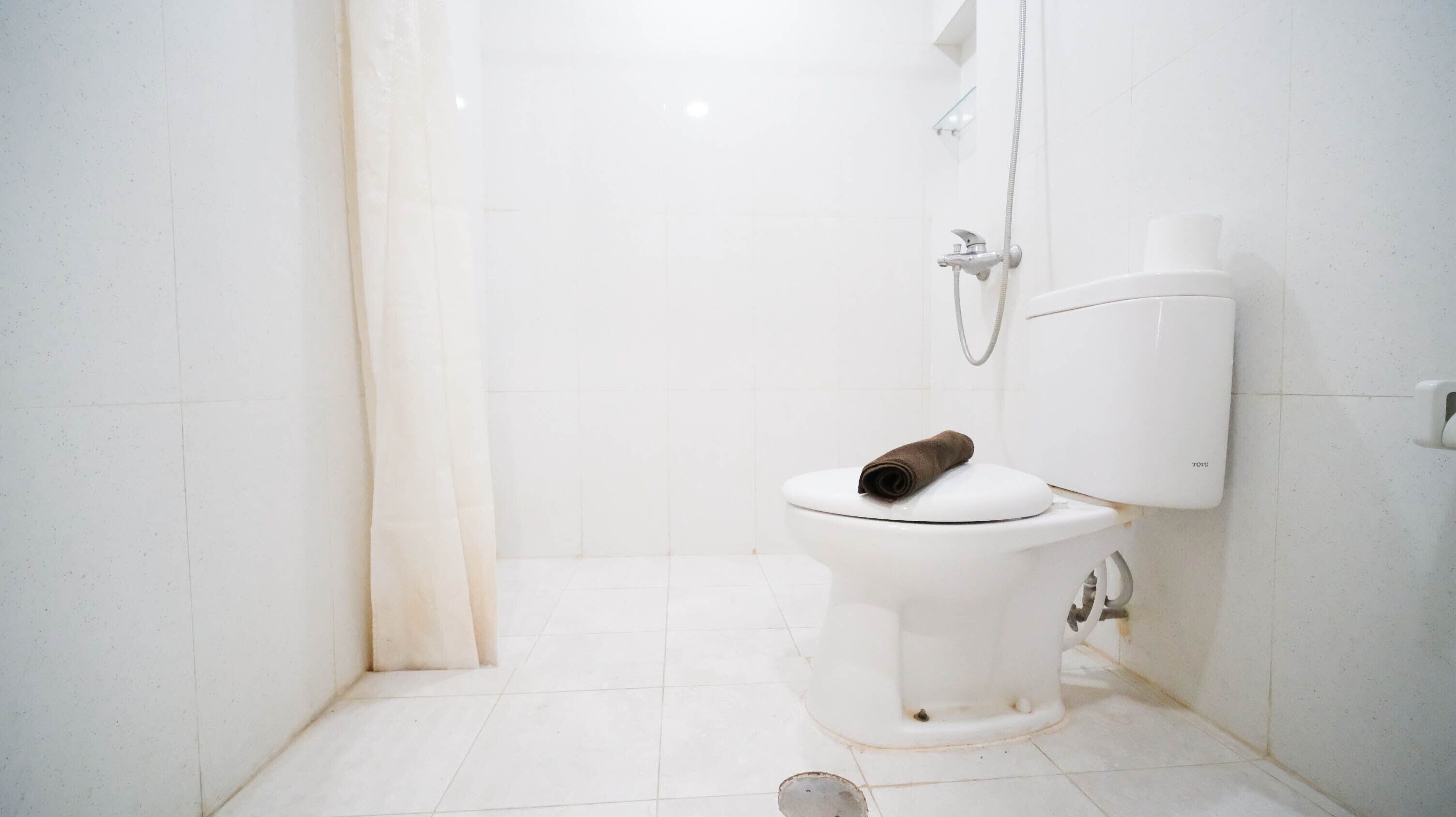 Une salle de bain avec des toilettes blanches, une douche et un porte-rouleau de papier toilette.