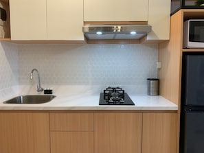 A kitchen with a stainless steel sink, a gas stove, wooden cabinets, and a microwave. - Nice Studio Room At Tokyo Riverside Pik 2 Apartment (Teluknaga)