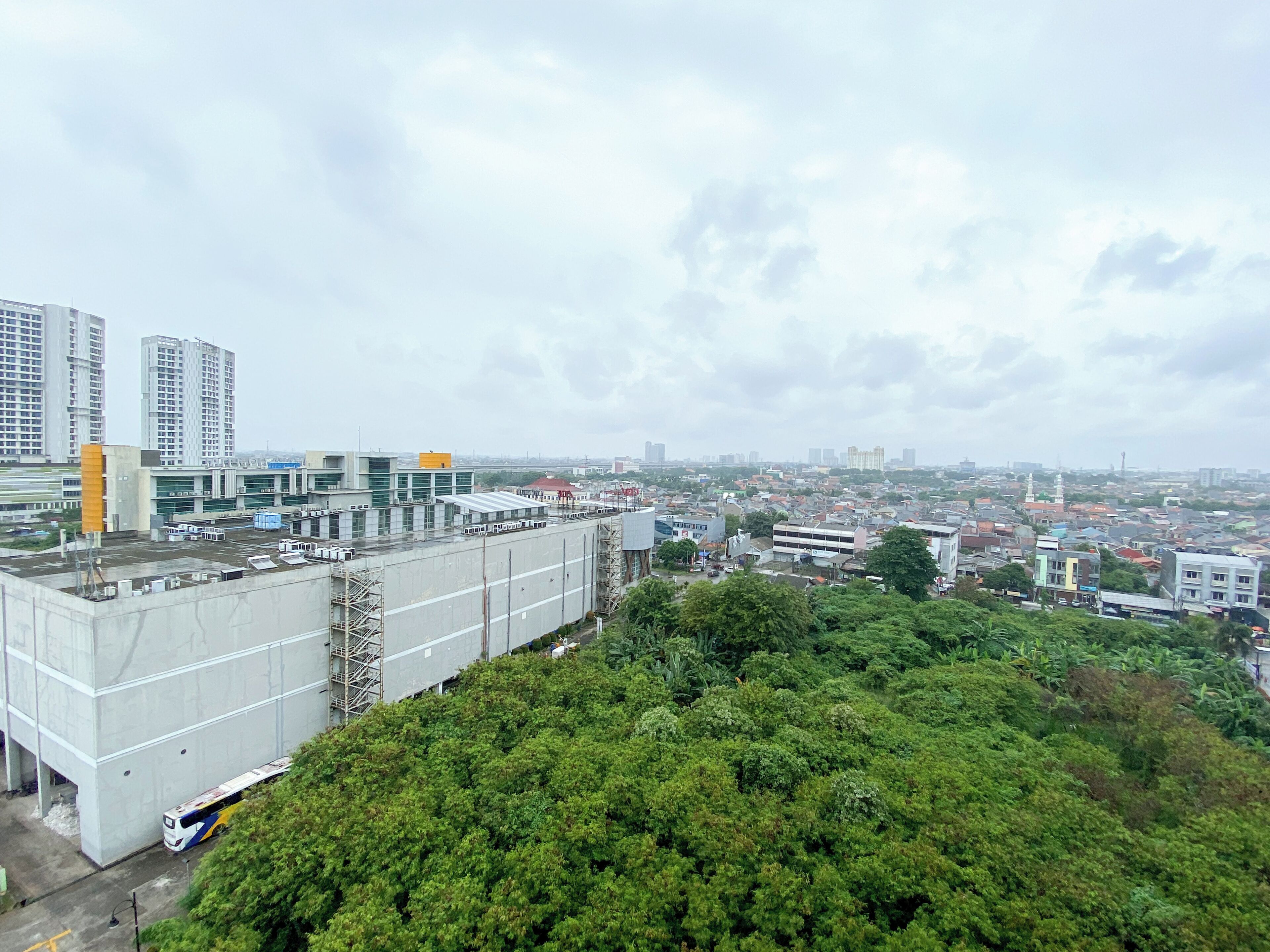 Un paisaje urbano con un edificio grande de techos planos y numerosas ventanas, rodeado de abundante vegetación.