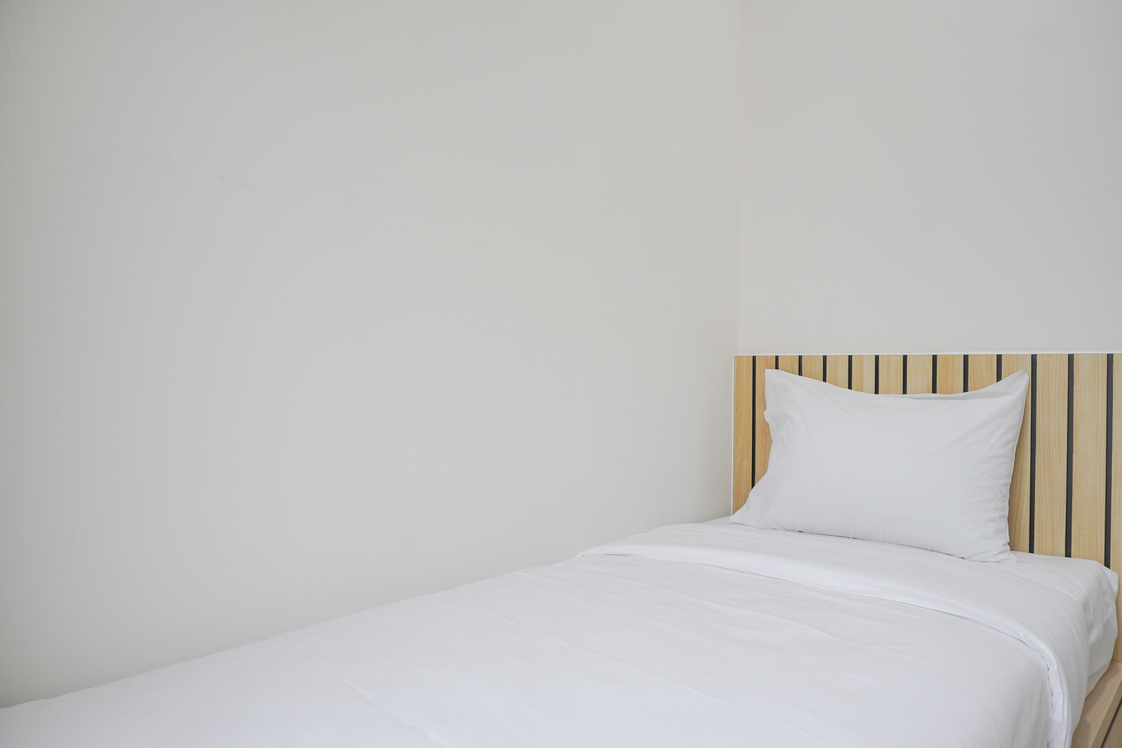 A single bed with a wooden headboard and white bedding in a room with plain white walls.