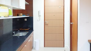 A compact kitchen with a black countertop, wooden cabinets, a sink, and a door with a handle. - Nice And Comfortable Studio At Vida View Makassar (Makassar)