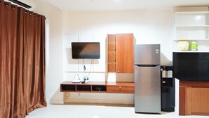 A modern kitchen with a flat-screen TV, wooden cabinets, a stainless steel refrigerator, and a microwave. - Nice And Comfortable Studio At Vida View Makassar (Makassar)