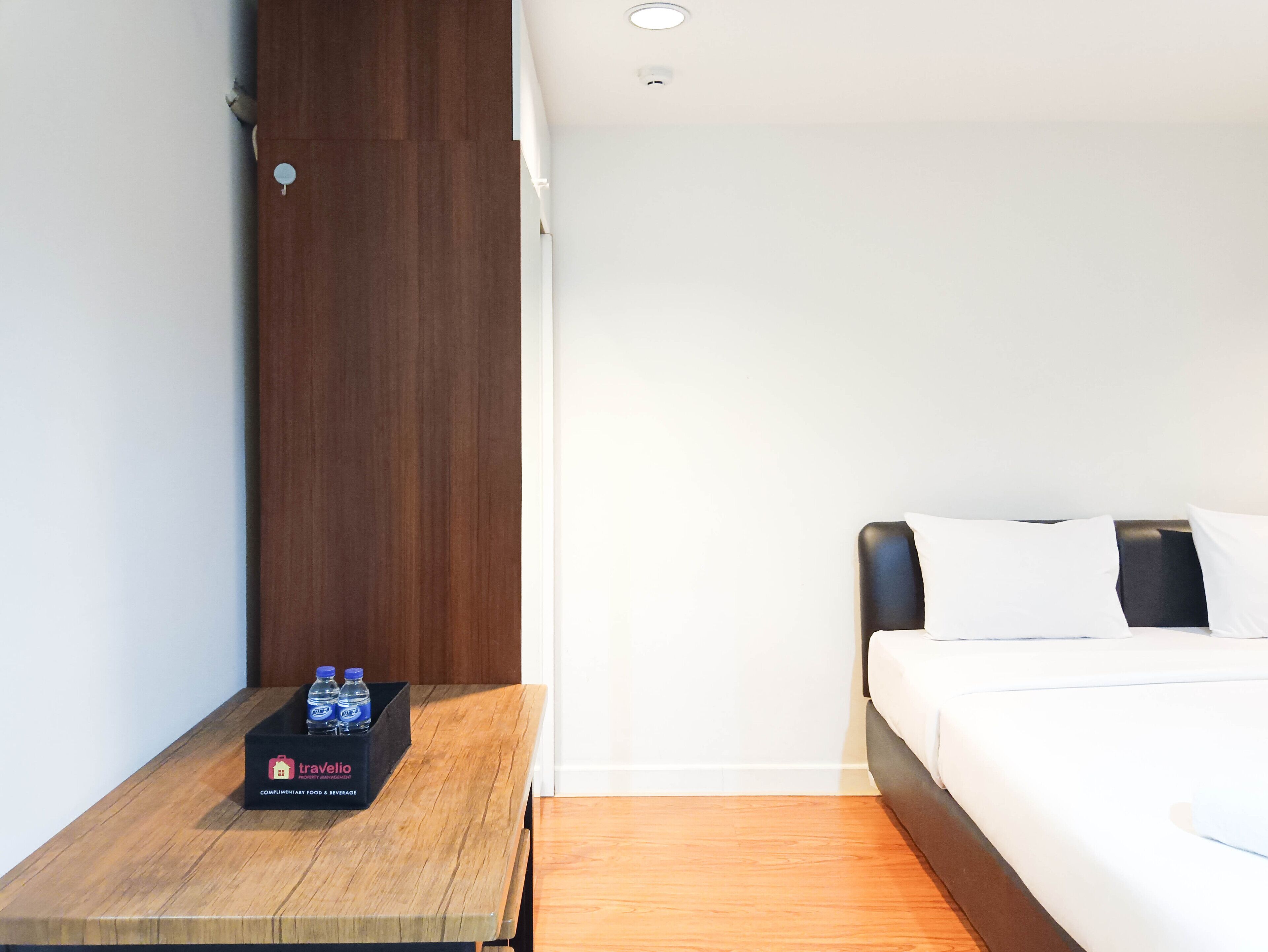 Una habitación de hotel con una mesita de noche de madera, una cama con ropa blanca y un piso de madera.