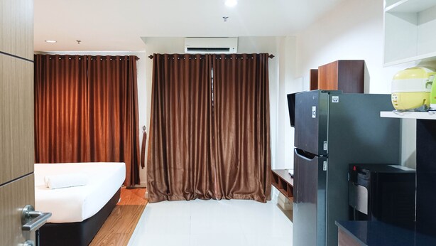 A compact hotel room with a bed, a small kitchenette, a refrigerator, and a window with curtains. - Nice And Comfortable Studio At Vida View Makassar (Makassar)