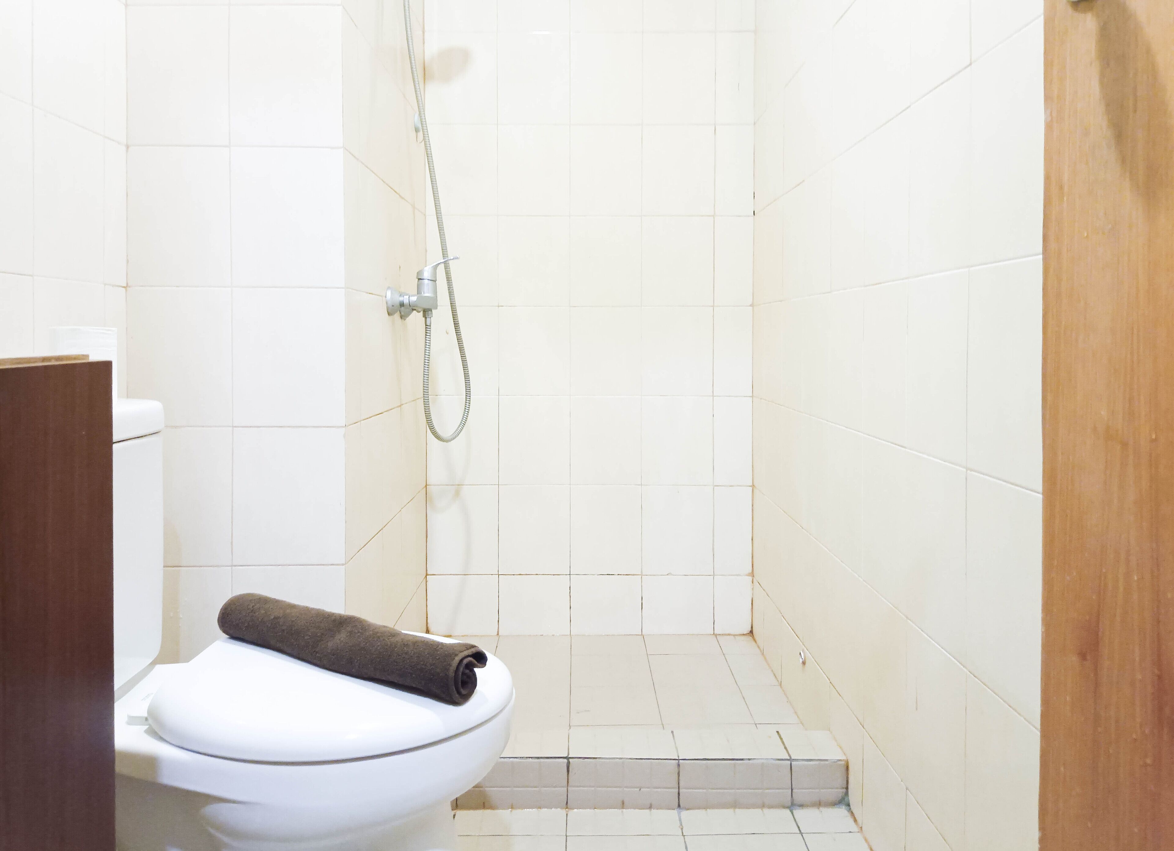 A small, clean bathroom with a toilet, a shower, and a wooden door.
