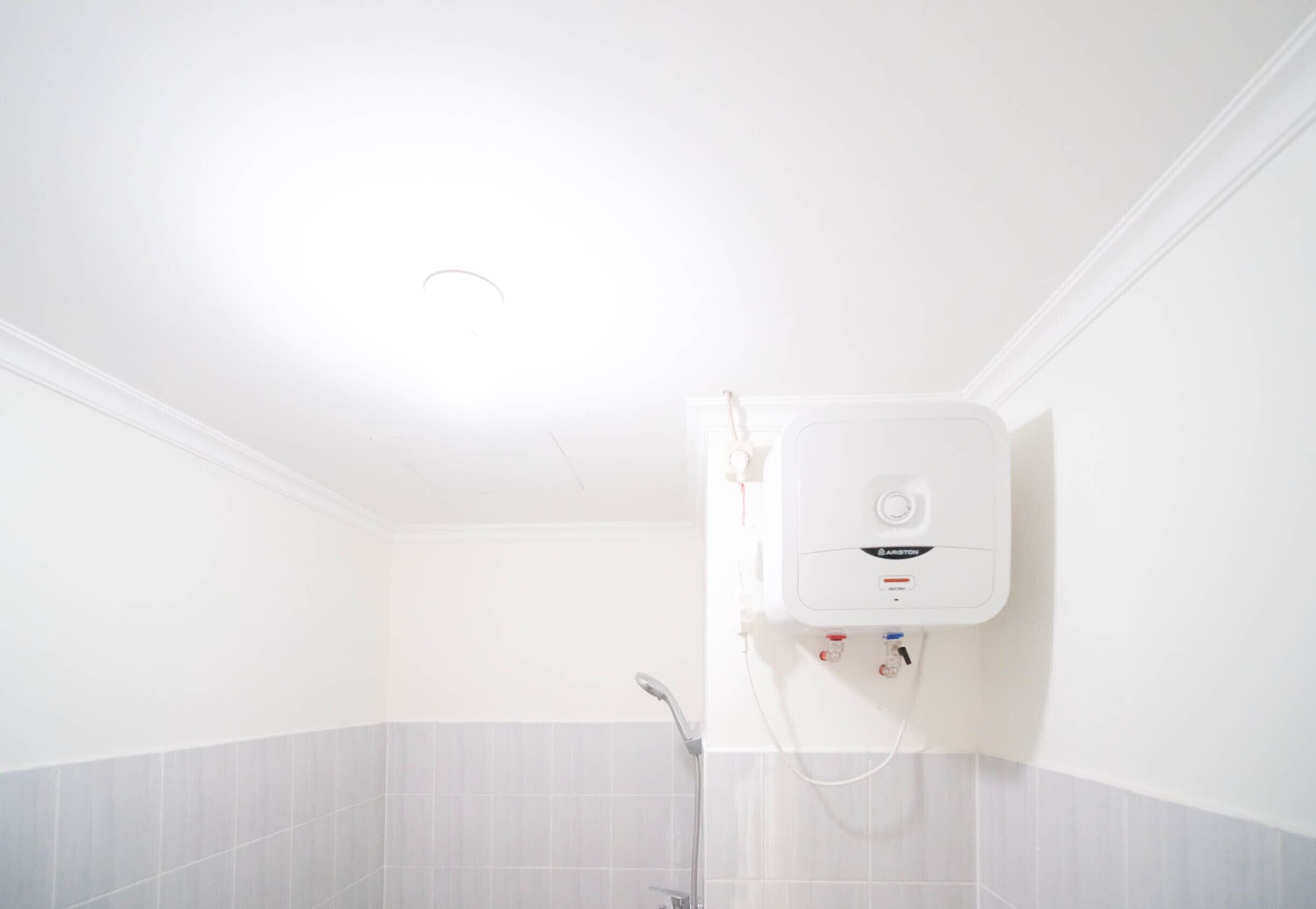 Ein Badezimmer mit Dusche, weißen Fliesen und einem an der Wand montierten Warmwasserbereiter.