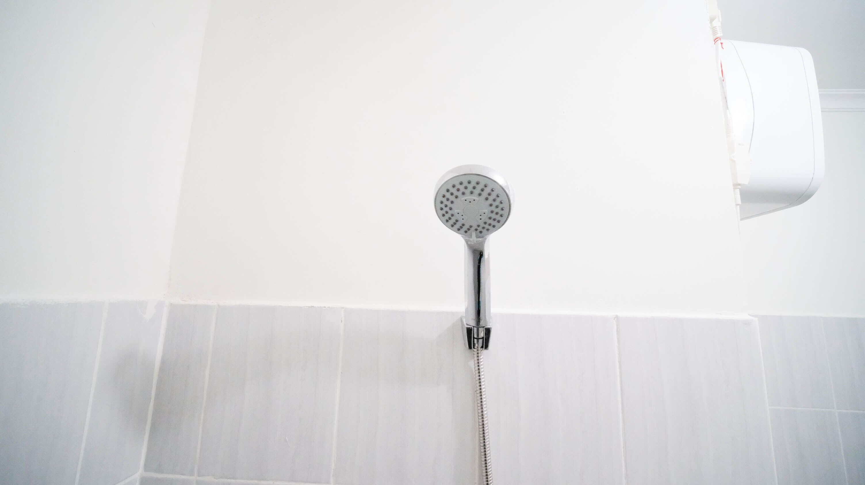 A showerhead mounted on a white tiled wall with a flexible hose.