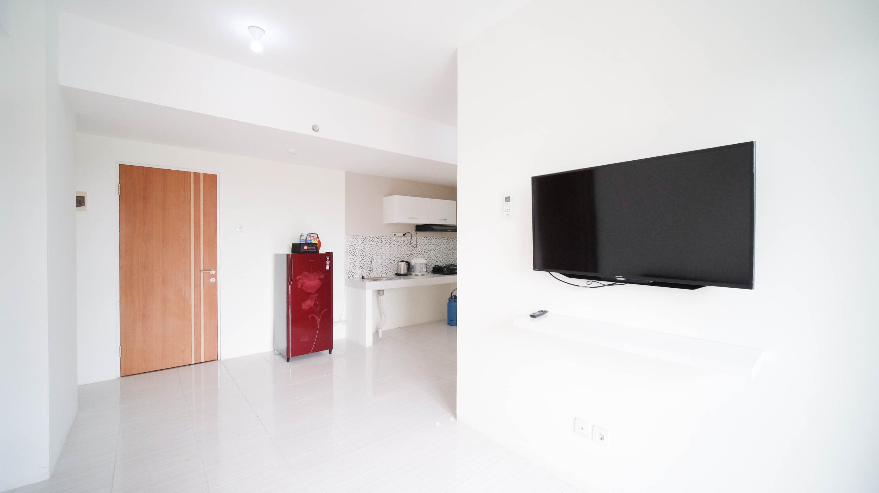 A modern kitchen with white cabinets, a red refrigerator, and a flat-screen TV mounted on the wall.