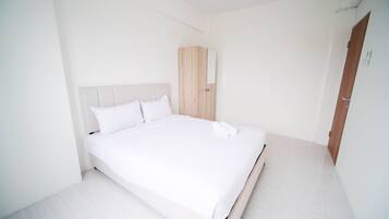 A clean, white room with a bed, a wooden wardrobe, and a door.