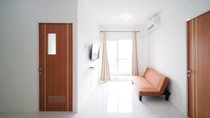A modern hotel room with a wooden door, a sofa, a TV mounted on the wall, and a large window with curtains. - Best Choice And Tidy 2Br At Puncak Dharmahusada Apartment (Surabaya)