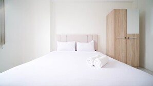 A neatly made bed with white linens and pillows, a wooden wardrobe with a mirror, and a plain white wall. - Best Choice And Tidy 2Br At Puncak Dharmahusada Apartment (Surabaya)