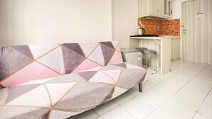 Een moderne woonkamer met een bank, een keukenhoek met een betegelde spatwand en een deur.