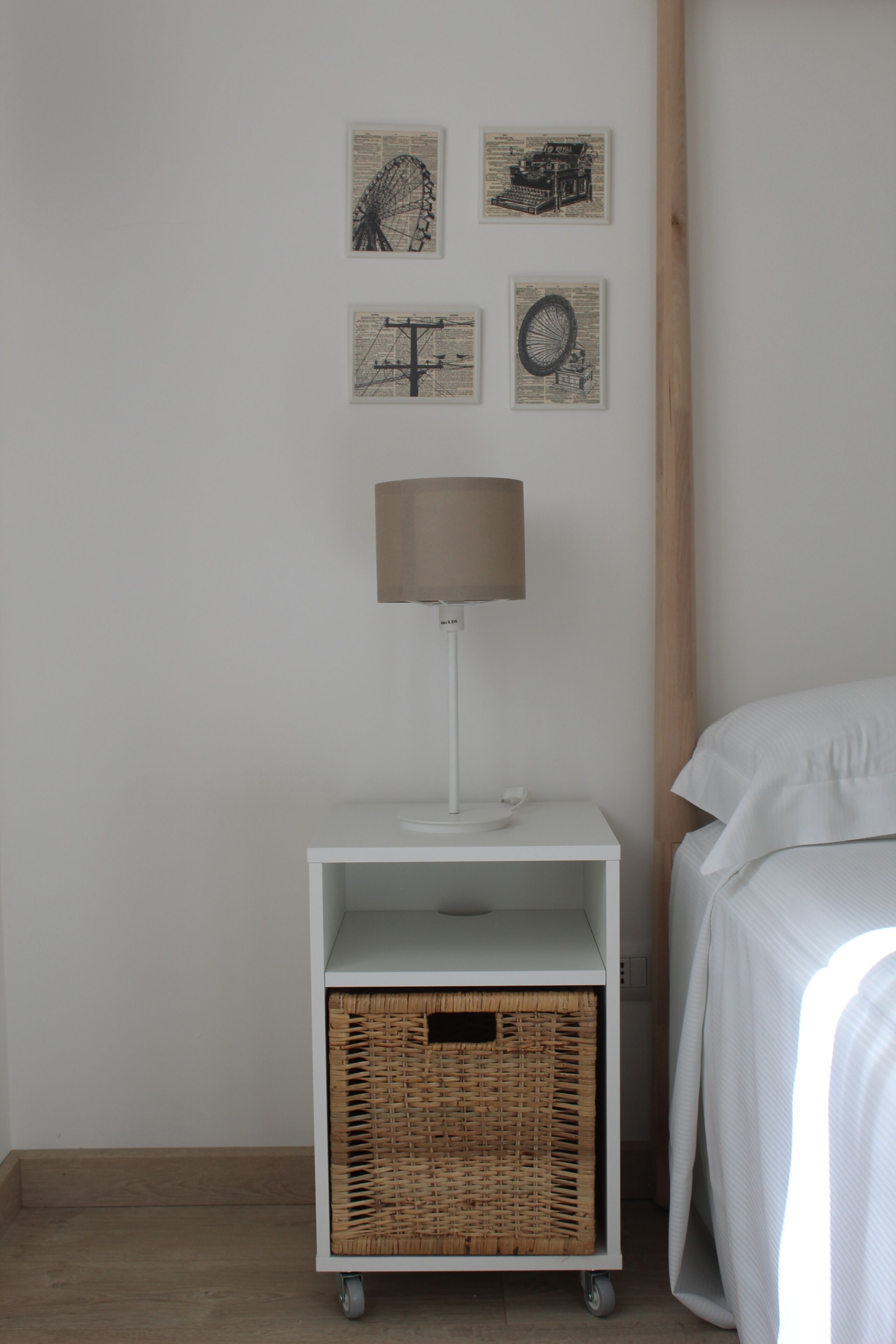 A bedroom with a bed, a nightstand with a lamp, a wicker basket, and four framed pictures on the wall.