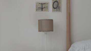 A bedroom with a bed, a nightstand with a lamp, a wicker basket, and four framed pictures on the wall.