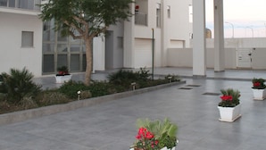 A modern building with multiple floors, large windows, and a central courtyard with potted plants and a tree. - Virgilio 82 - Penthouse With Terrace (Trapani)