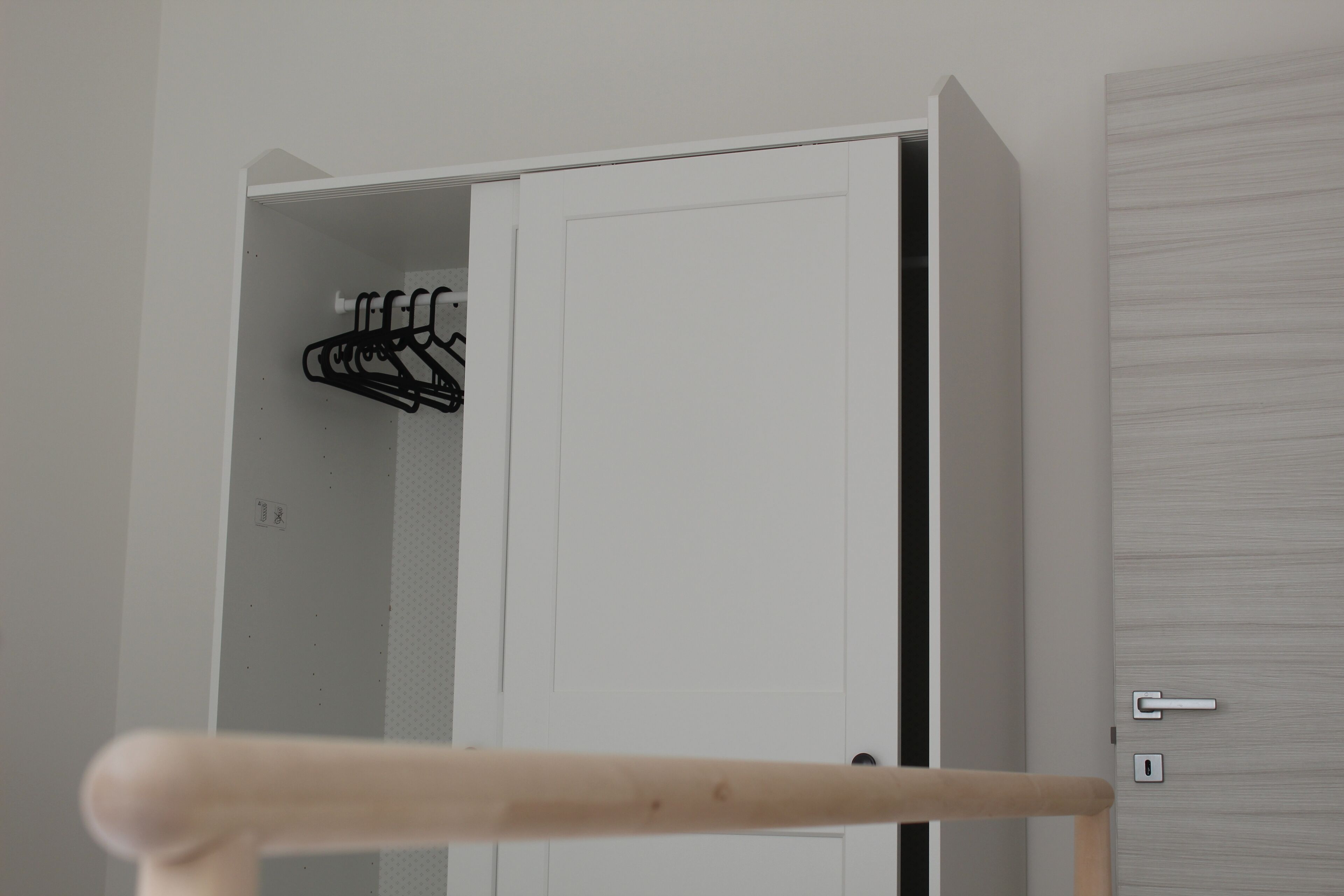 A white door with a metal handle and a keyhole, a wooden door frame, and a black coat rack with hangers.