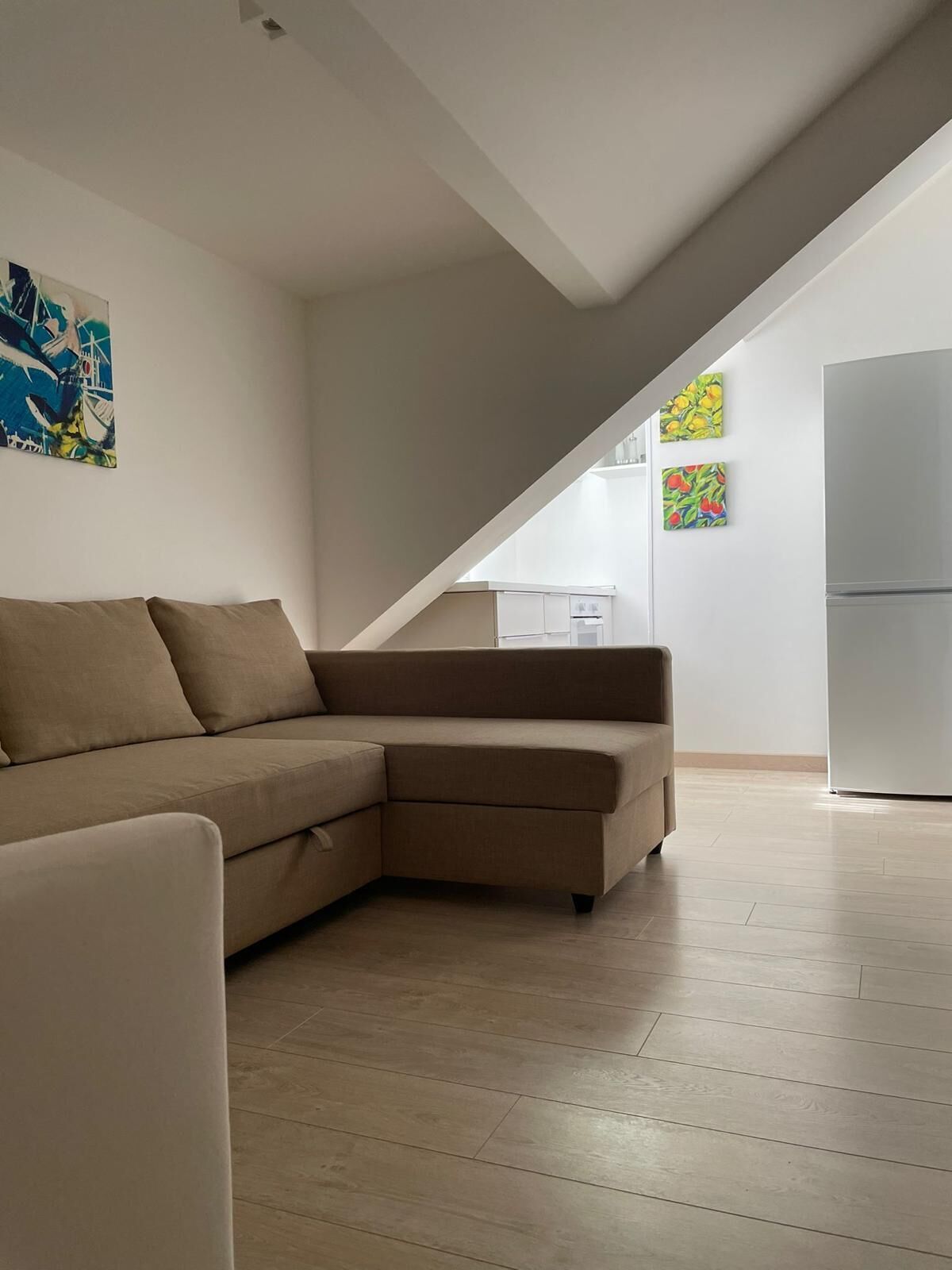 A modern living room with a sectional sofa, a dining area with a table and chairs, and a kitchen with a refrigerator.