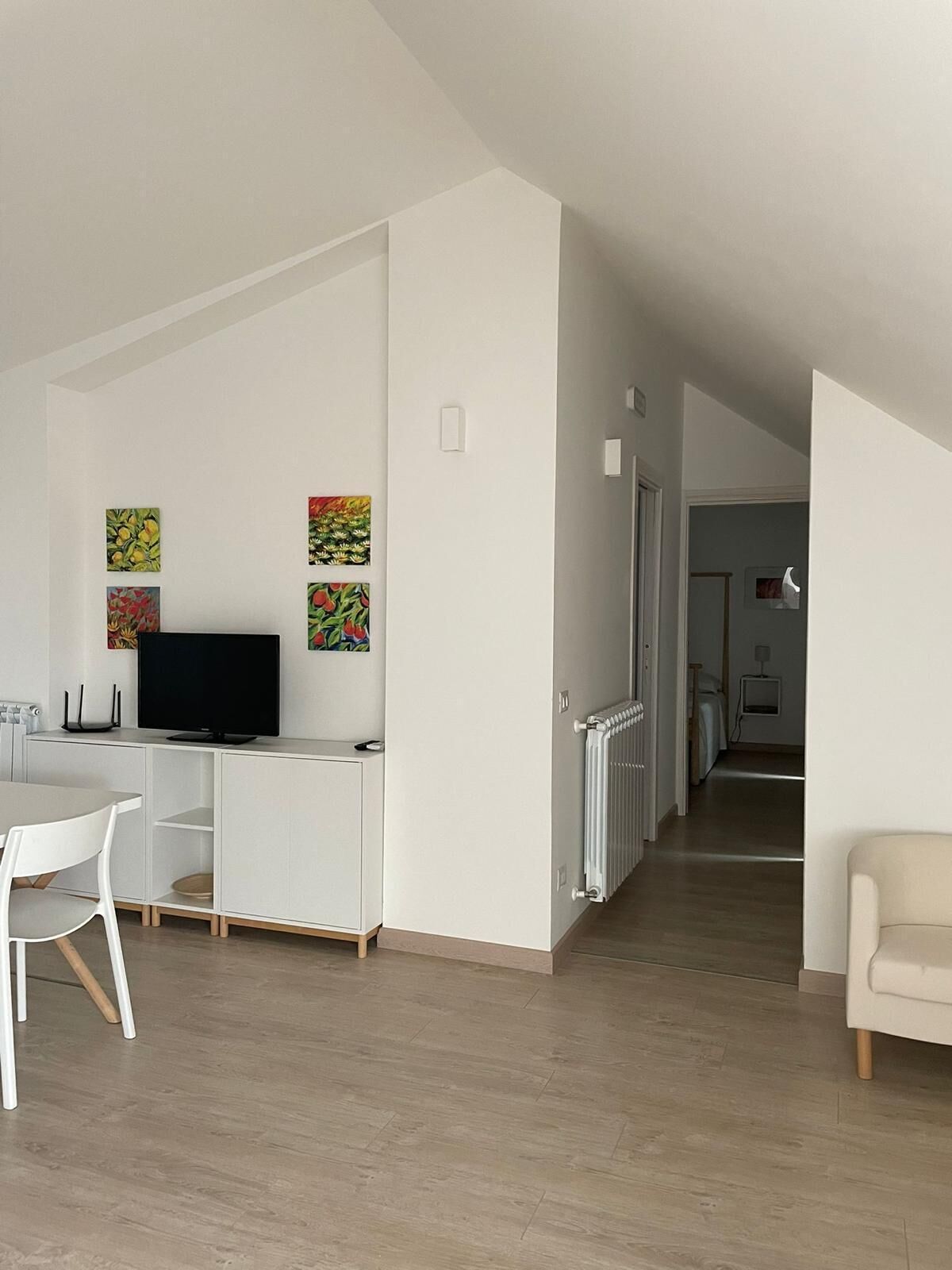 Una sala de estar moderna con televisor de pantalla plana, muebles blancos y obras de arte en las paredes.