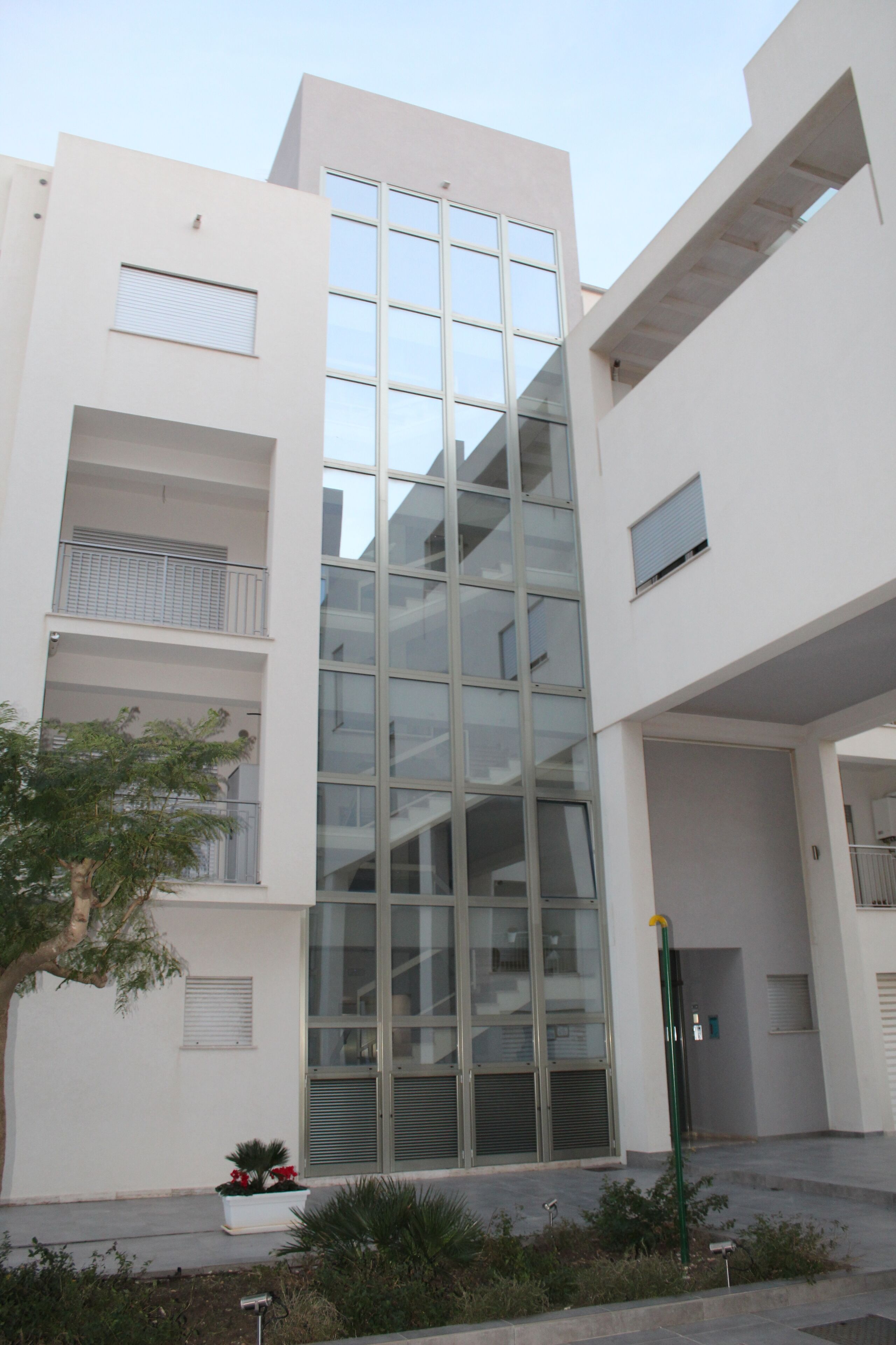 Un edificio moderno con fachada de vidrio central, varios balcones y techo plano.