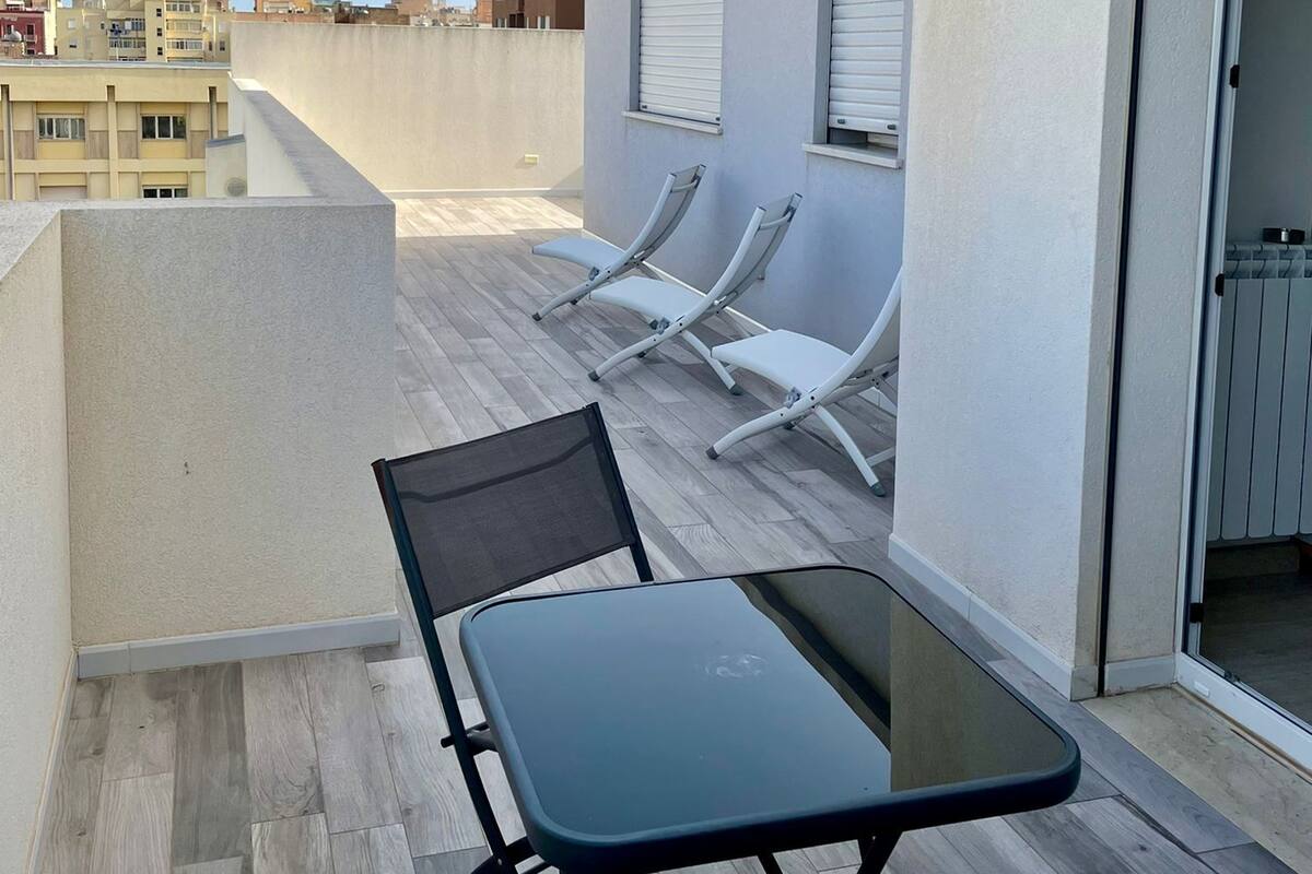 A rooftop terrace with a table and chairs, a sliding door, and a view of the cityscape.