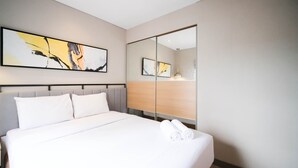 Habitació d'hotel amb un llit gran, un capçal de llit, un mirall i dos quadres abstractes a la paret.