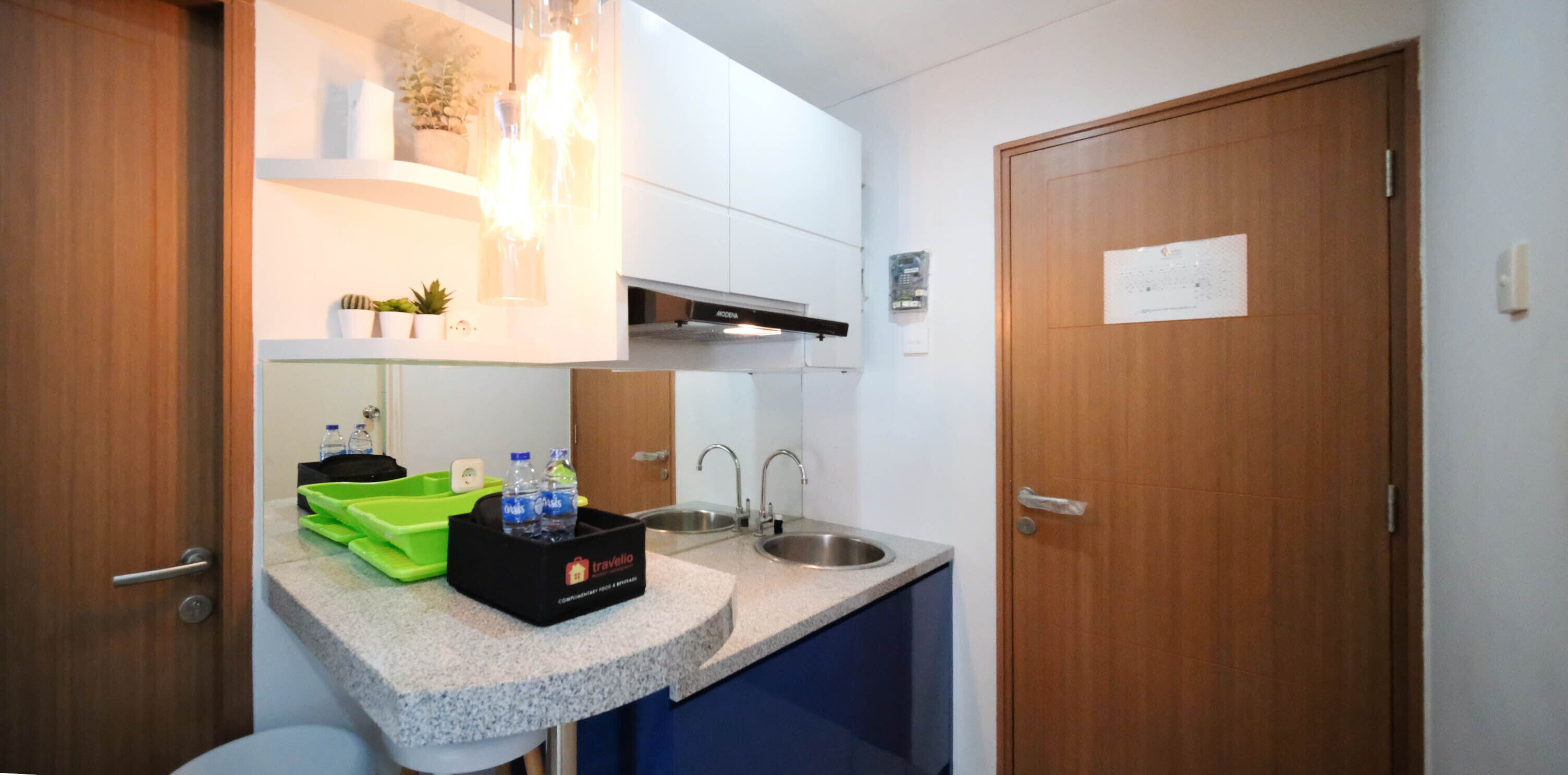 A compact kitchenette with a sink, countertop, and a small cabinet. There are two bottles of water and a green tray on the counter.