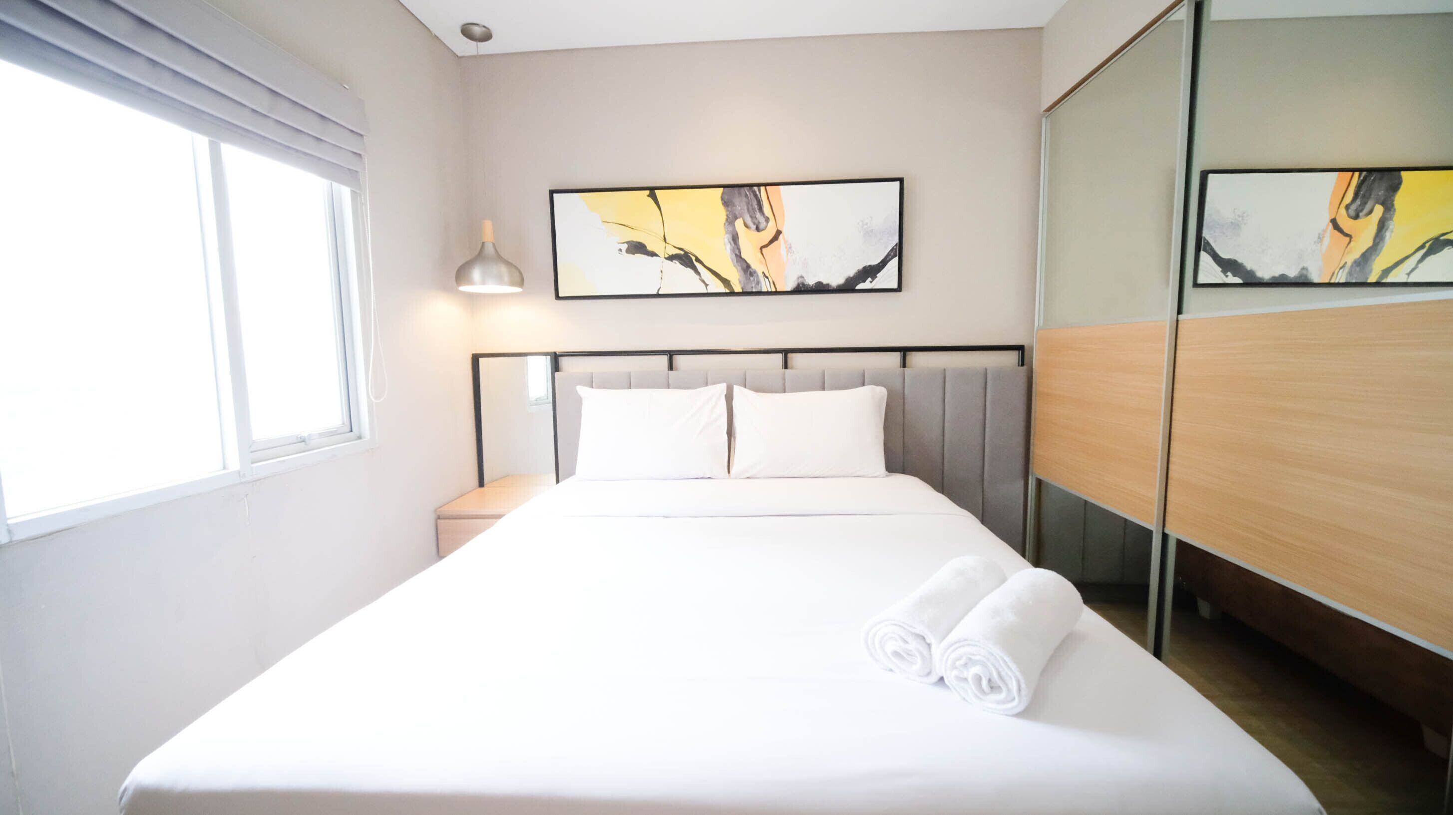 A hotel room with a large bed, a nightstand, a lamp, and artwork on the wall.