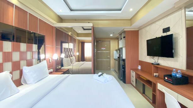 A hotel room with a large bed, a desk, a TV, and a mirror.