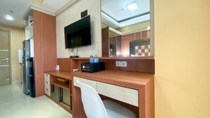 A hotel room with a wooden desk, a white chair, a flat-screen TV mounted on the wall, and a minibar.