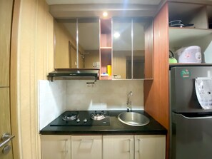 A compact kitchen with a gas stove, sink, and a refrigerator. - Cozy Studio Room At Oasis Cikarang Apartment (Cikarang)