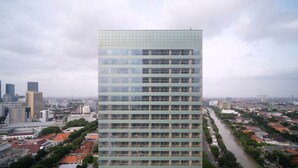 Ein modernes Hochhaus mit Glasfassade, umgeben von einer Mischung aus Wohn- und Geschäftshäusern, und ein Fluss, der durch die Stadt fließt.