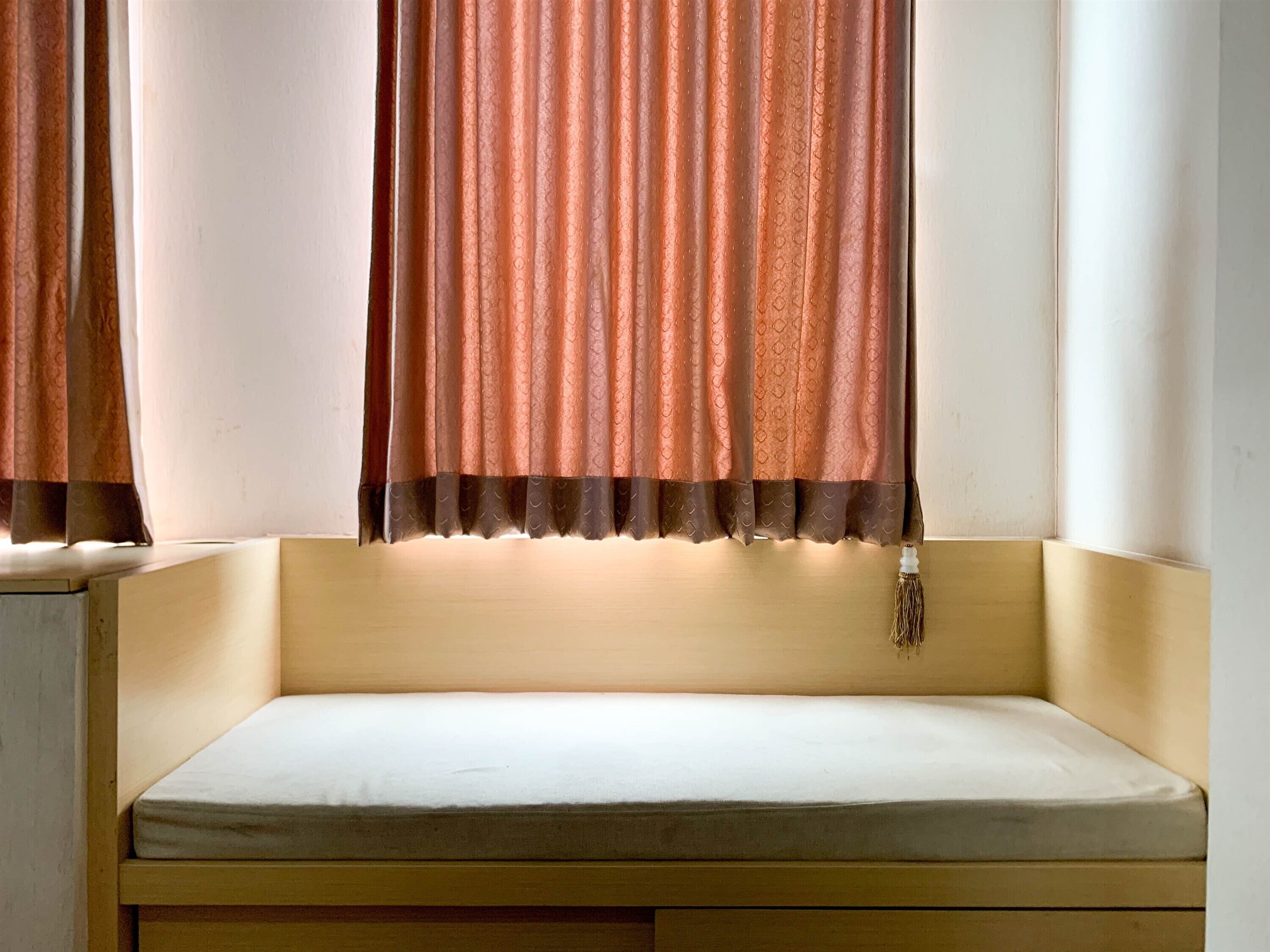 A small, cozy room with a single bed, a window with curtains, and a bedside table with a lamp.