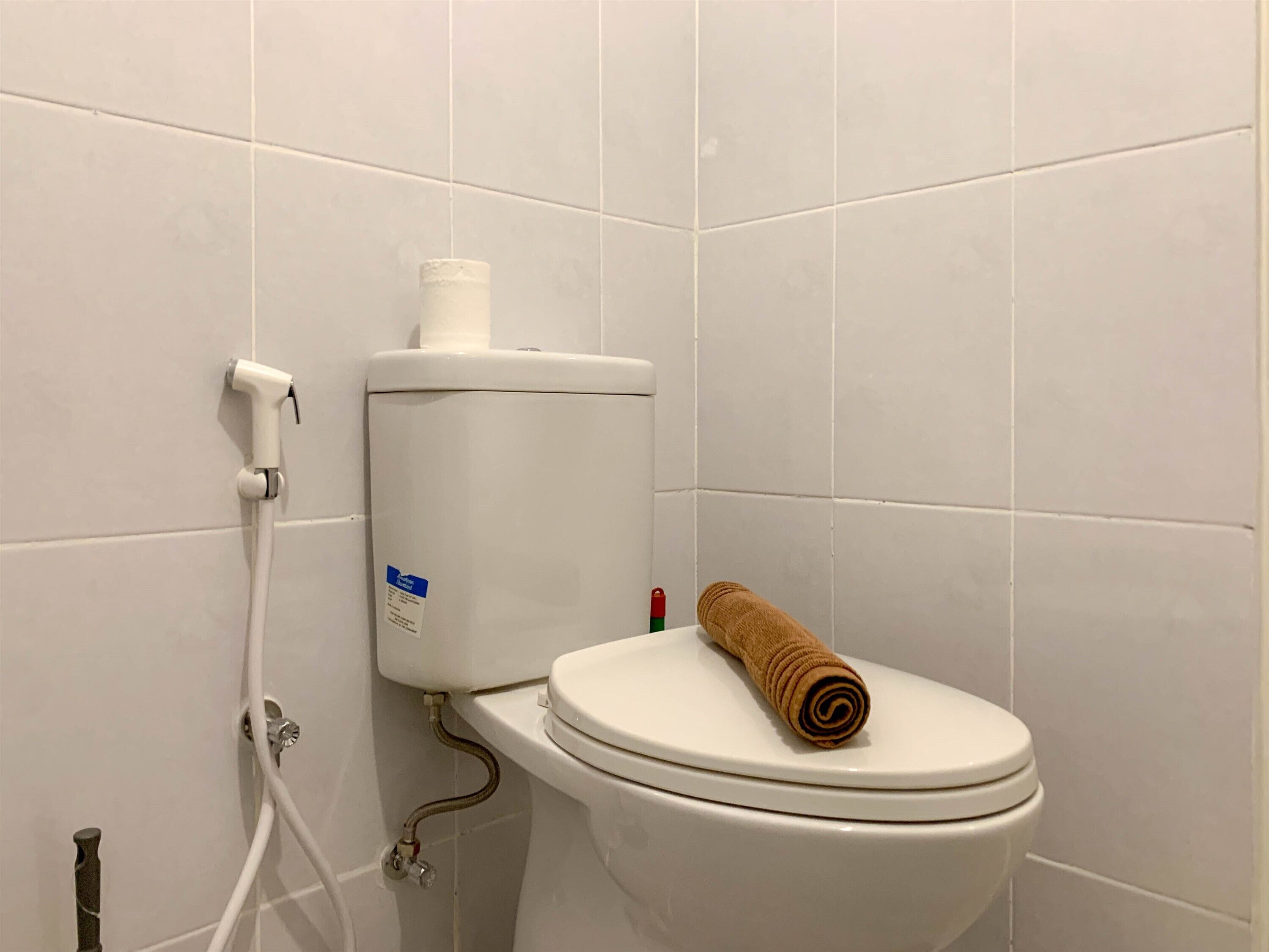 A toilet with a white tank, a roll of toilet paper, and a towel on the seat.