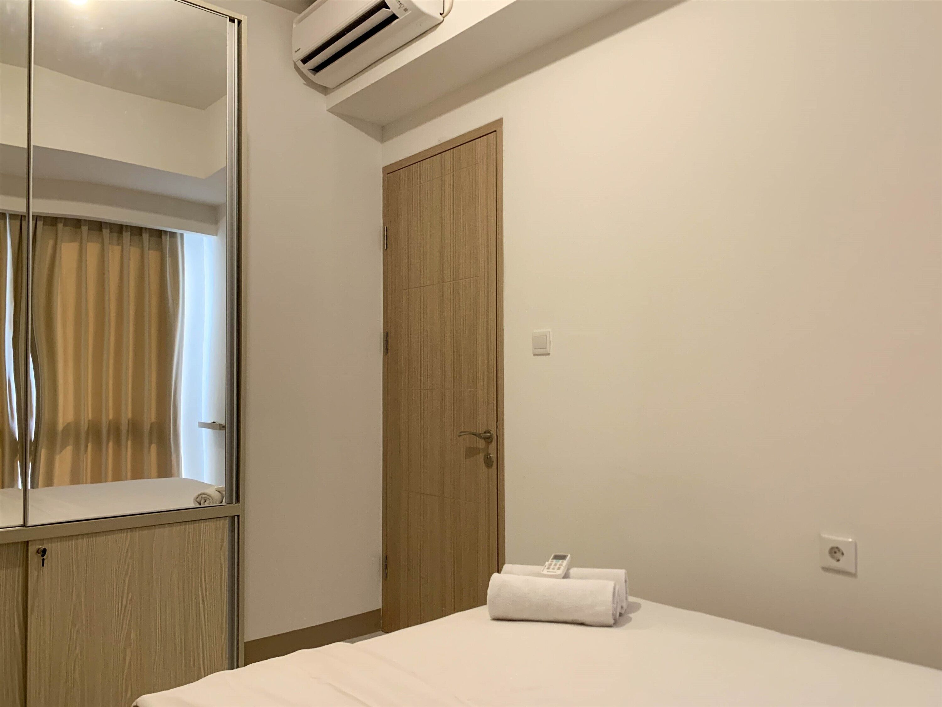 Ein Hotelzimmer mit einem Bett, einem Holzschrank, einem Spiegel, einer Klimaanlage, einer Tür und einem Handtuch auf dem Bett.