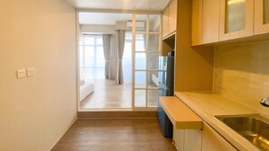 A narrow kitchen with a built-in refrigerator, a sink, and a window overlooking a balcony. - Cozy And Simple Big Studio Vasanta Innopark Apartment (Cikarang)