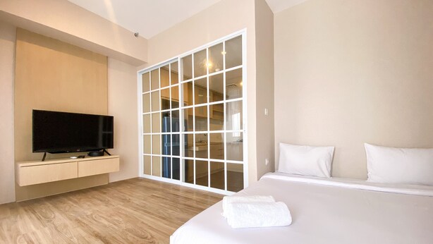 A modern hotel room with a large bed, a flat-screen TV mounted on a wall, and a sliding glass door leading to a kitchen area. - Cozy And Simple Big Studio Vasanta Innopark Apartment (Cikarang)