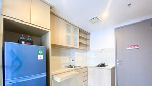 A compact kitchen with a blue refrigerator, a sink, and wooden cabinets. - Cozy And Simple Big Studio Vasanta Innopark Apartment (Cikarang)
