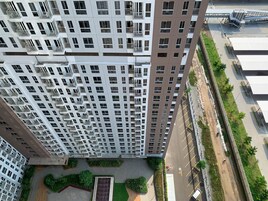 A high-rise building with multiple balconies and a parking area with green landscaping.