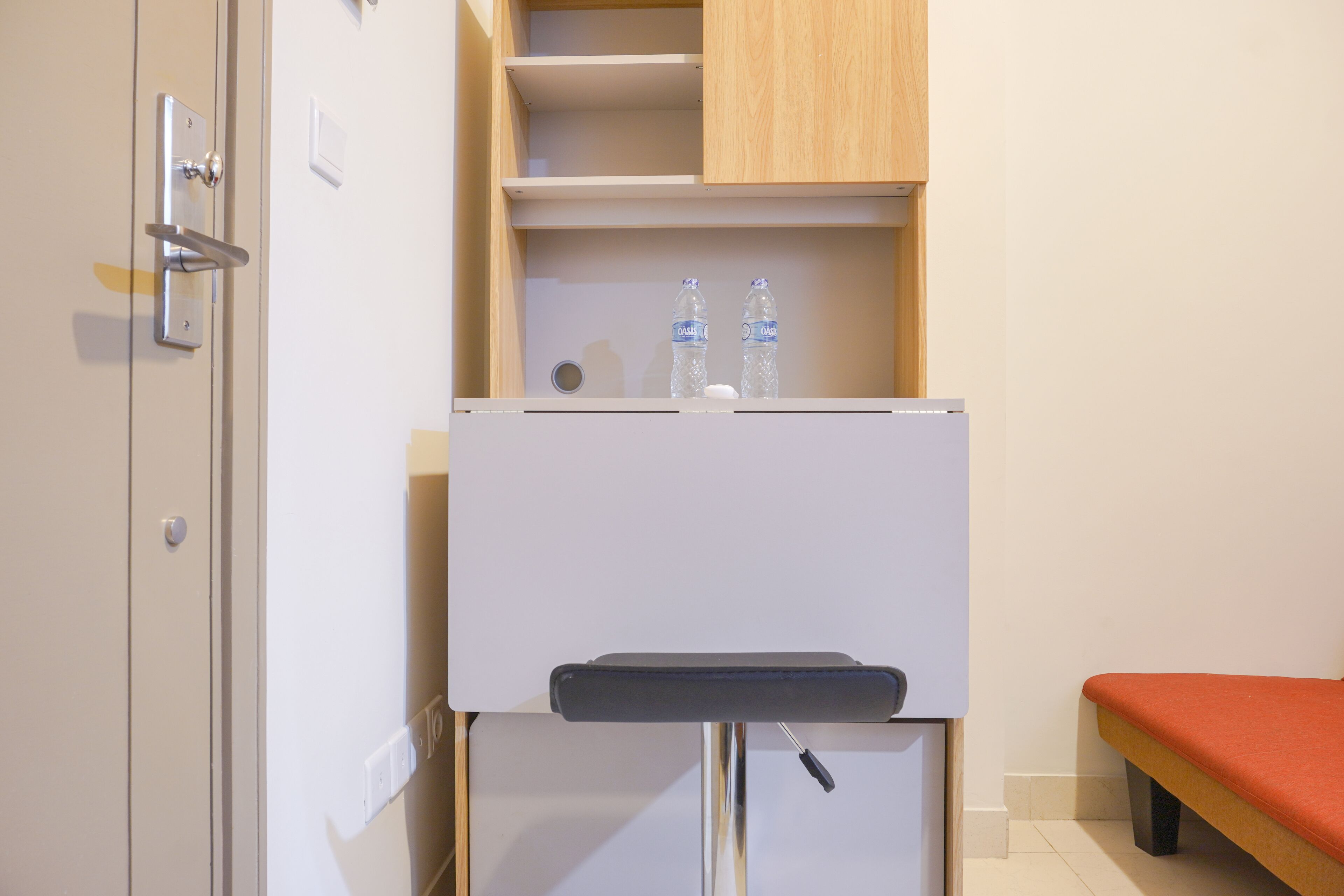 A compact room with a white minibar, a wooden cabinet above it, and a small bench to the right.