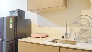 Eine Küche mit Kühlschrank, einer rosa Waage, einem Spülbecken mit Geschirrständer und beigen Schränken.
