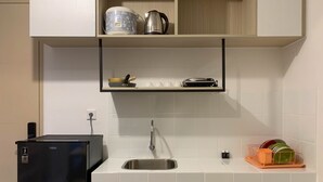 Cocina compacta con refrigerador negro, pileta y encimera con escurridor y tabla de cortar.